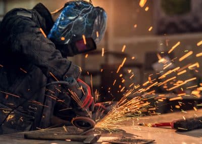 Fitzgerald Metal Works. Man in welding suit and helmet providing Welding Services at a work bench.