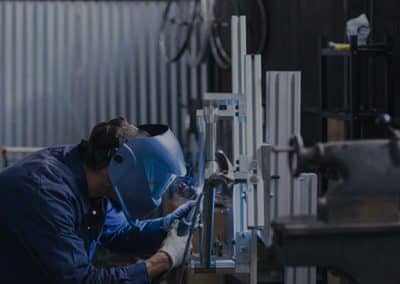 Worker in a blue Welding suit and blue helmet. Welding pieces of metal together at a work bench