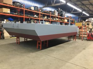 Fitzgerald Metal Works. A red and grey boat hull in a workshop, positioned on stands for stability.