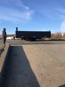 Fitzgerald Metal Works. Large black barge on trailer being brought down a ramp