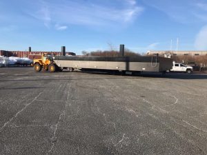 Fitzgerald Metal Works. A large flat-bottomed barge being towed by a yellow tractor in an industrial area.