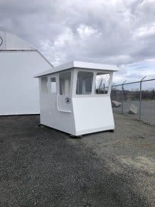 Fitzgerald Metal Works. White Barge Cabin sitting outdoors in a fenced in area awaiting assembly