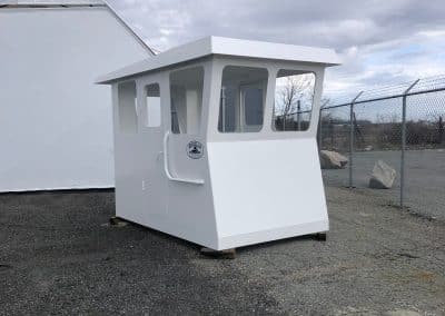 Fitzgerald Metal Works. White Barge Cabin sitting outdoors in a fenced in area awaiting assembly