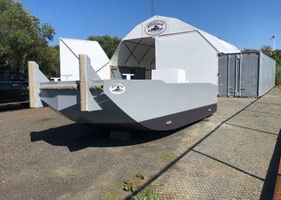 Fitzgerald Metal Works. A large, gray barge with a white tent and a shipping container in the background, parked on a gravel lot.