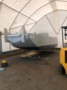 Fitzgerald Metal Works. A large, gray barge, parked on a gravel lot inside of an industrial tent.