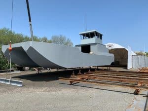 Fitzgerald Metal Works. Large grey barge on stilts in an industrial yard. Steel beam being lifted by a crane onto barge.