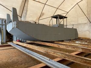 Fitzgerald Metalworks. A grey A metal workboat or utility vessel inside a tent-like structure, suggesting it is being built, repaired, or maintained.