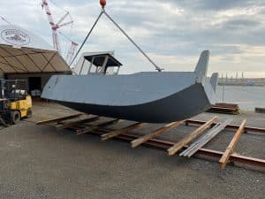 Fitzgerald Metalworks. A barge vessel being lifted or moved within an outdoor boatyard.