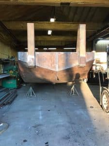 Fitzgerald Metal Works. The interior of a workshop where a rusty metal boat hull is being constructed or repaired.