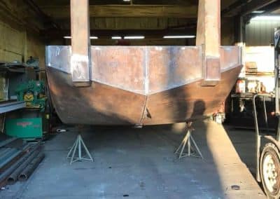 Fitzgerald Metal Works. The interior of a workshop where a rusty metal boat hull is being constructed or repaired.