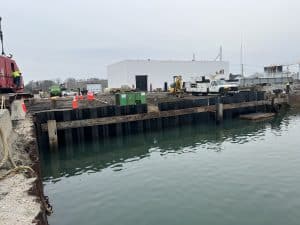 Fitzgerald Metalworks. Marine Construction. Black metal sheets line the waters edge. Buildings, cars and machines located in the background.