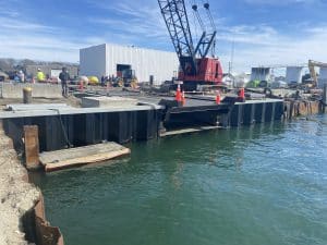 Fitzgerald Metalworks. A large red crane, traffic cones, marine construction worker beside and above a body of water