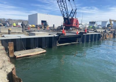 Fitzgerald Metalworks. A large red crane, traffic cones, marine construction worker beside and above a body of water