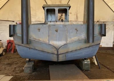 Fitzgerald Metal Works. The stern view of a grey barge on wooden supports in a work area tent