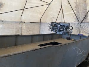 Fitzgerald Metal Works. Barge engine suspended by a chain in the air in a workshop tent