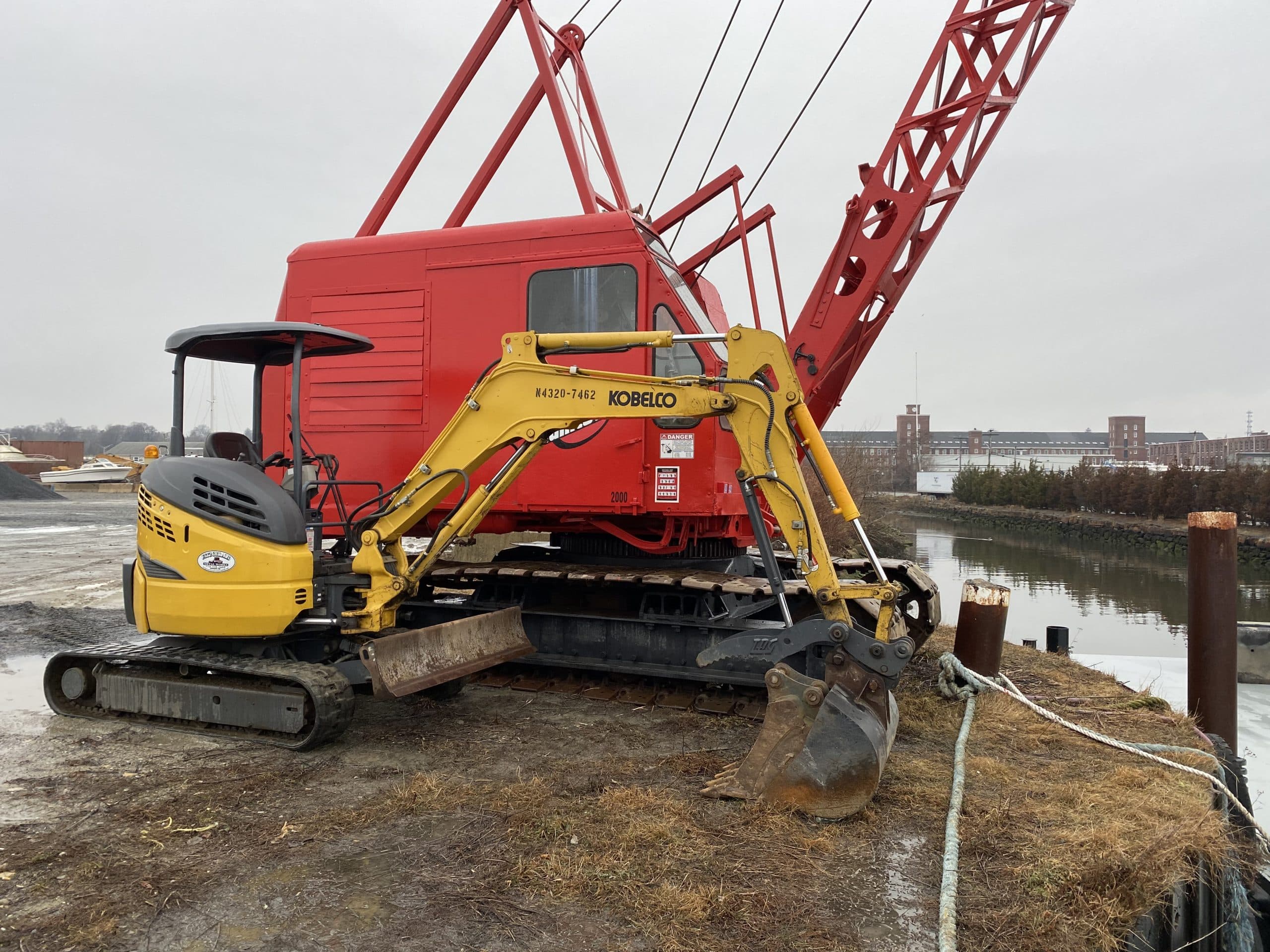 Fitzgerald Metalworks. Red crane and yellow tractor by a body of water.