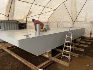 Fitzgerald Metalworks. Marine fabrication professional working on the surface of a barge in a work area tent.