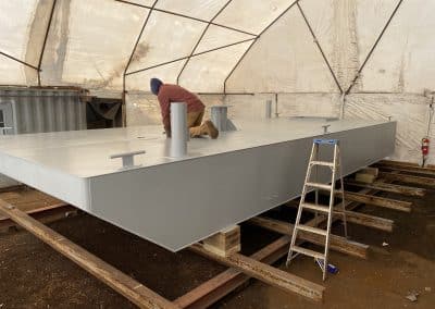 Fitzgerald Metalworks. Marine fabrication professional working on the surface of a barge in a work area tent.