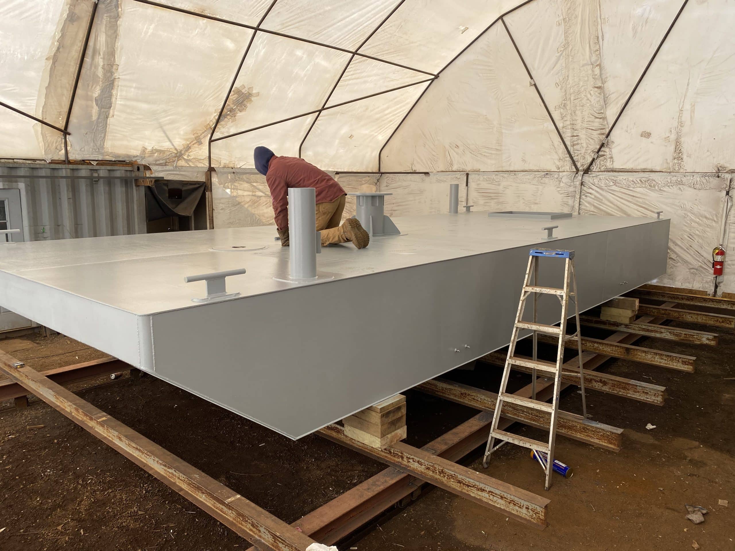 Fitzgerald Metalworks. Marine fabrication professional working on the surface of a barge in a work area tent.