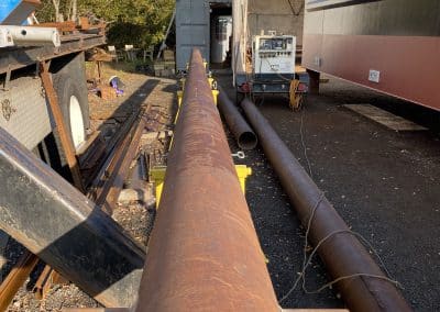 Fitzgerald Metalworks. Rusty brown Pipe in the center of image surrounded by other rusty pipes and a truck. Fitzgerald Metalworks.