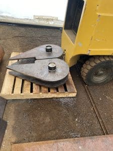 Fitzgerald Metalworks. A close-up of two large, teardrop-shaped metal components placed on a wooden pallet in a workshop or construction area.