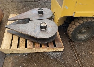 Fitzgerald Metalworks. A close-up of two large, teardrop-shaped metal components placed on a wooden pallet in a workshop or construction area.