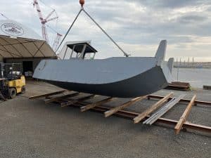 Fitzgerald Metalworks. a barge vessel being lifted by a crane within an outdoor boatyard.