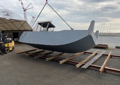 Fitzgerald Metalworks. a barge vessel being lifted by a crane within an outdoor boatyard.