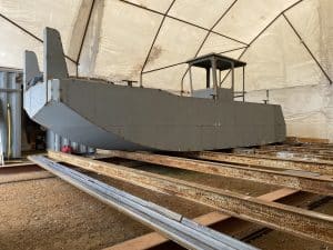 Fitzgerald Metalworks. A large grey barge under construction in a covered workshop area.