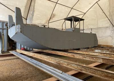 Fitzgerald Metalworks. A large grey barge under construction in a covered workshop area.