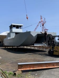 Fitzgerald Metalworks. A large grey catamaran-style barge vessel under construction in an outdoor boatyard.