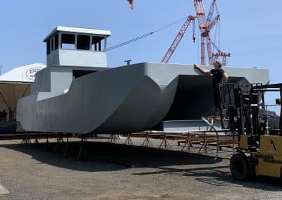 Fitzgerald Metalworks. A large grey catamaran-style barge vessel under construction in an outdoor boatyard.