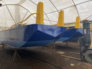 Fitzgerald Metalworks. Two catamaran-style barge boats under construction or maintenance in a covered workshop area.