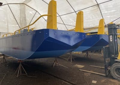 Fitzgerald Metalworks. Two catamaran-style barge boats under construction or maintenance in a covered workshop area.