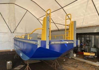 Fitzgerald Metalworks. The rear view of a barge, likely under construction or maintenance, in a covered workshop area in a tent