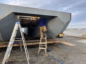 Fitzgerald Metalworks. A large metal barge or boat under construction by a Fitzgerald Metalworks worker