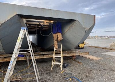 Fitzgerald Metalworks. A large metal barge or boat under construction by a Fitzgerald Metalworks worker