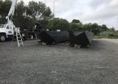 Fitzgerald Metal Works. Two large, newly constructed black barge hulls placed on wooden supports