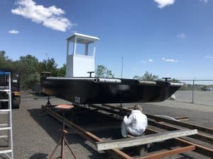 Fitzgerald Metal Works. Newly constructed barge with black hull and white cabin. Fitzgerald Metalworks worker seated under the barge.