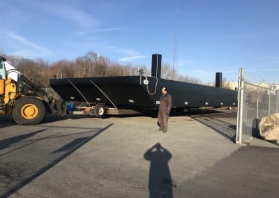 Fitzgerald Metal Works. A large black barge being moved on a trailer.