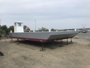 Fitzgerald Metal Works. a large, newly constructed barge boat hull on stands in a boat yard