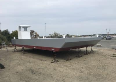 Fitzgerald Metal Works. a large, newly constructed barge boat hull on stands in a boat yard